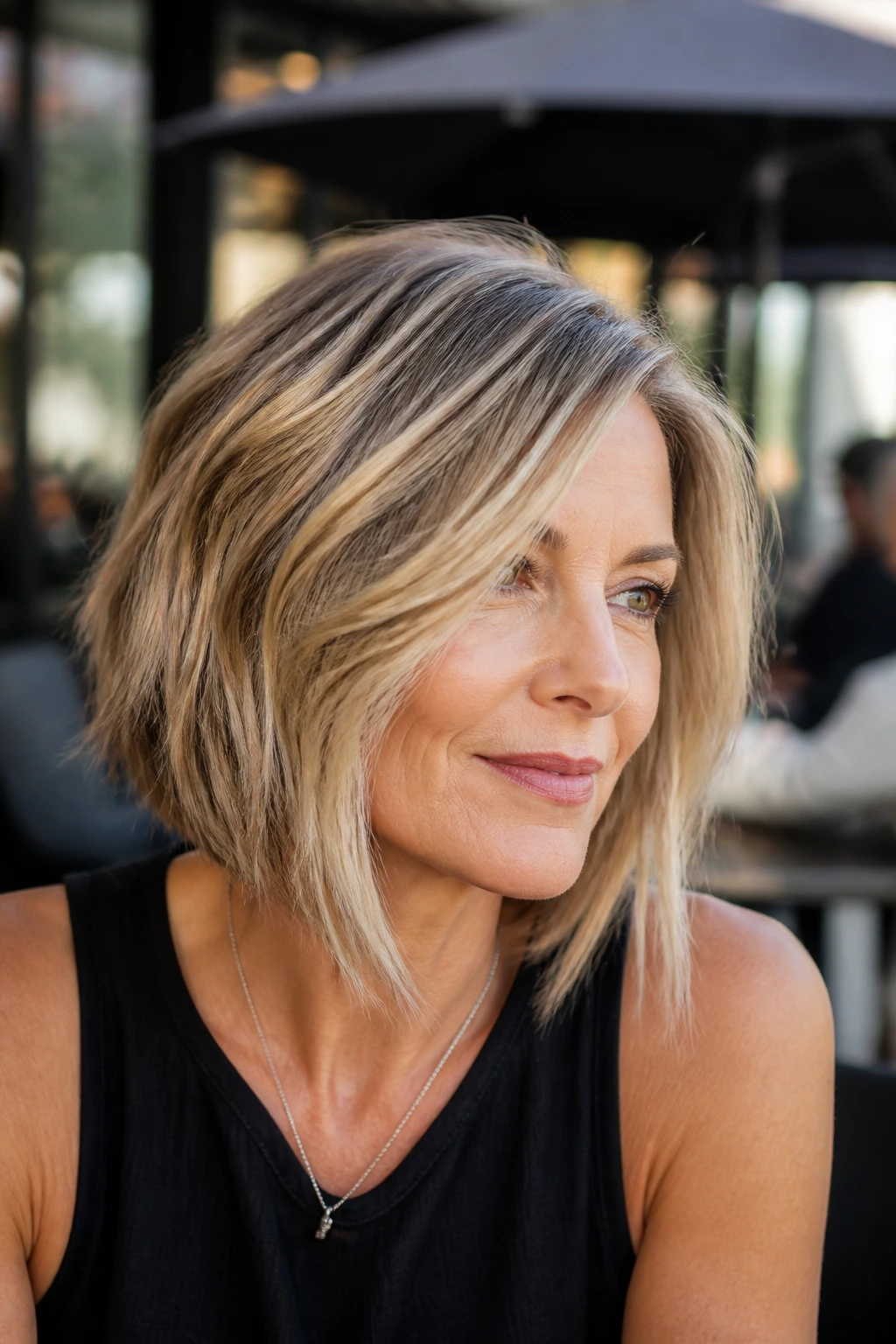 Portrait of a real woman with angled lob and choppy layers in daylight outdoor cafe.