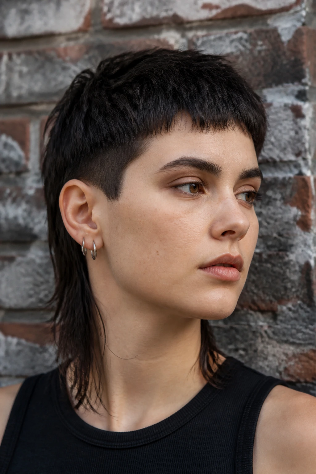 Close-up portrait of a real person with an asymmetrical mullet against an urban brick wall