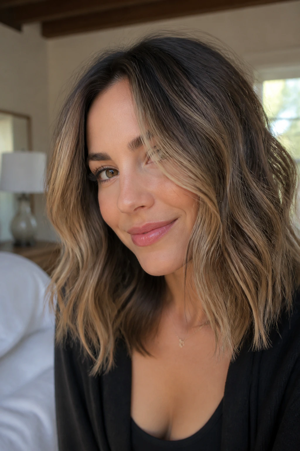 Close-up of a real woman with shoulder-skimming balayage on medium-length hair in warm window light