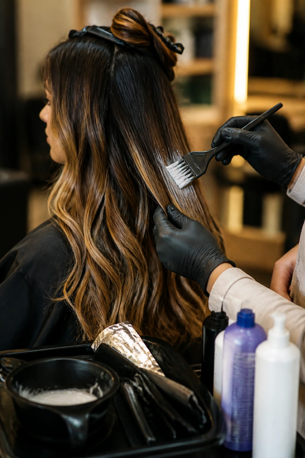 Close-up in-salon shot showing a stylist applying product to mid-length ombre hair
