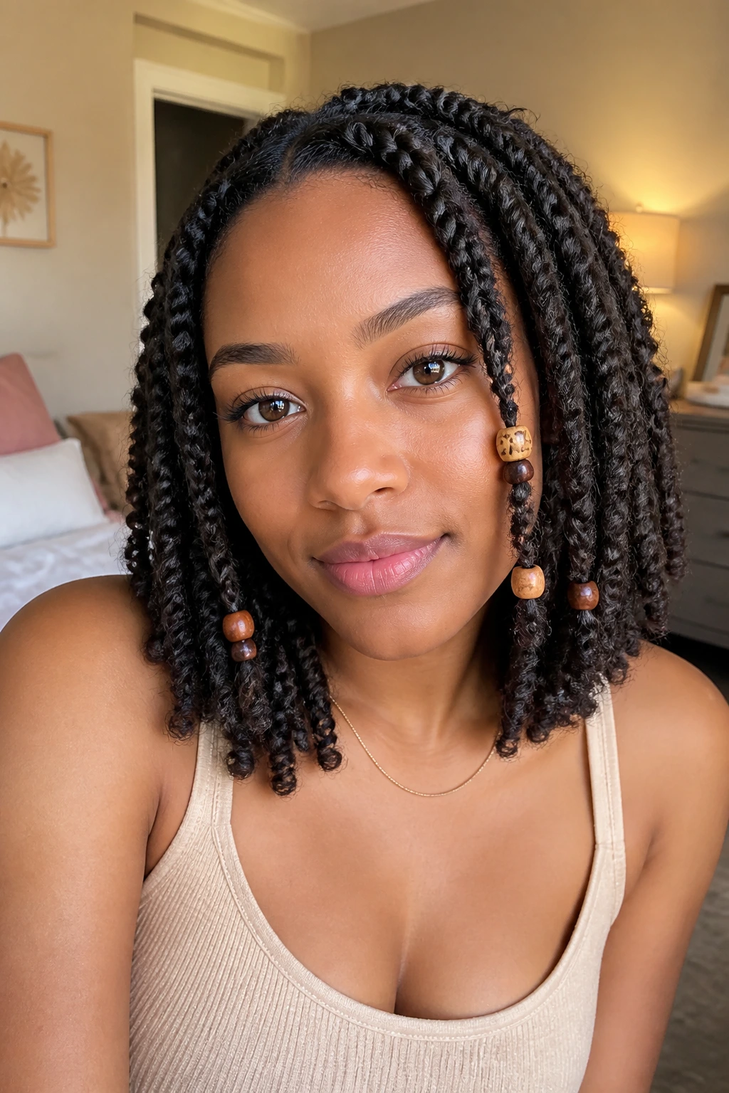 Close-up of a woman with beaded spring twists in a softly lit bedroom