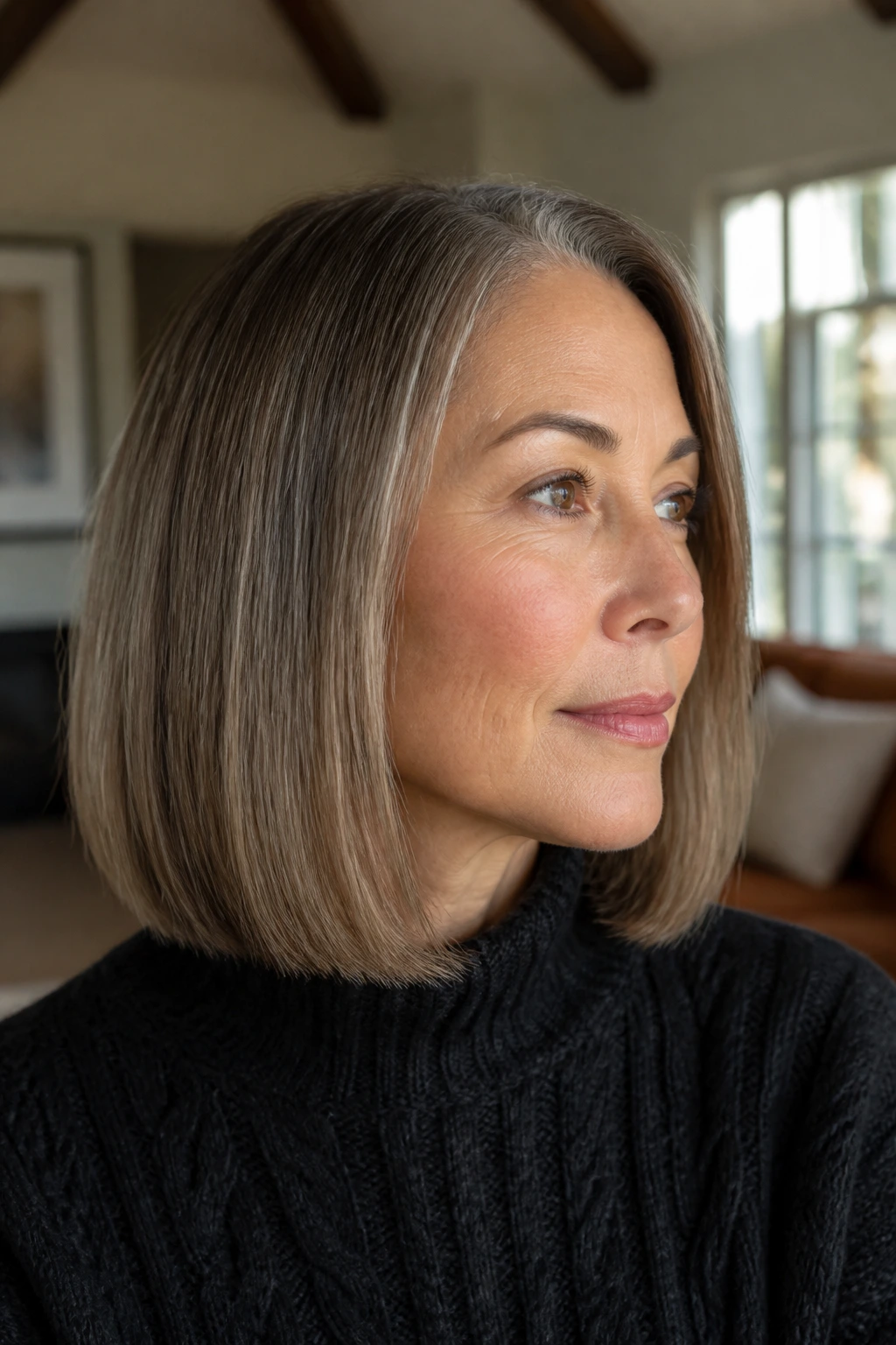 Close-up of a real woman with a blunt beige-brunette lob and gray blending at the temples in soft window light