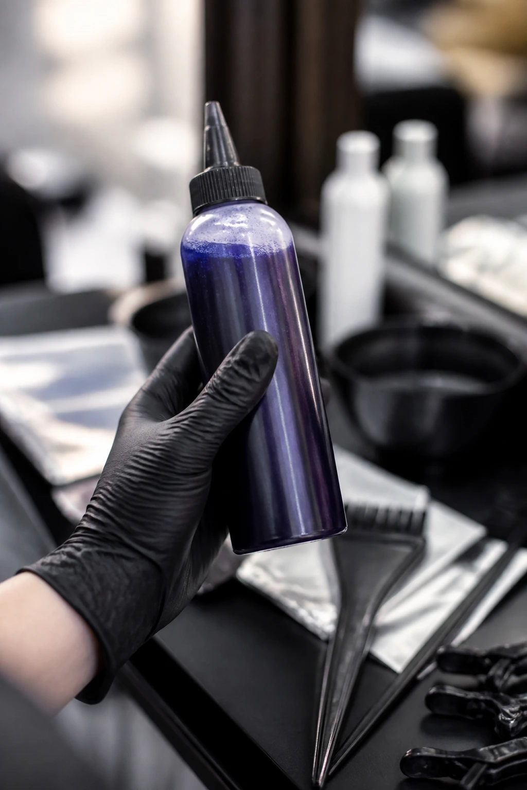 Close-up of gloved hand holding blue-violet toner bottle in salon
