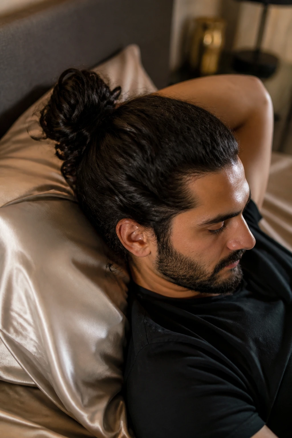 Man with bun in a bedroom scene near a satin pillowcase