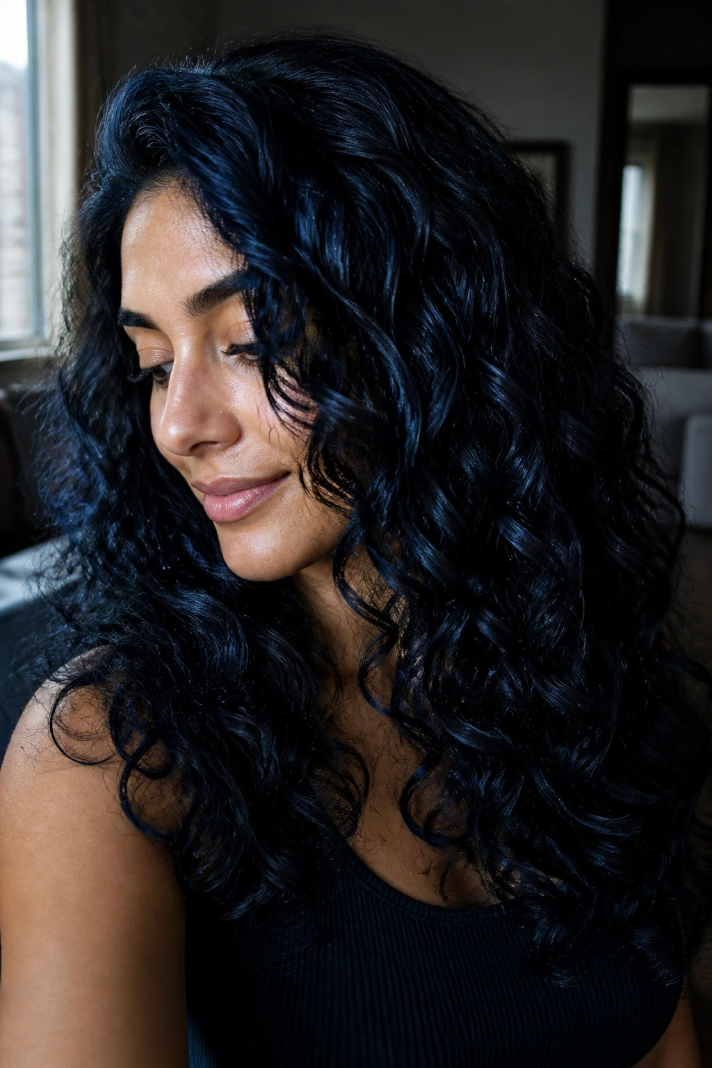 Blue-black shiny curls on a real woman in a dim room