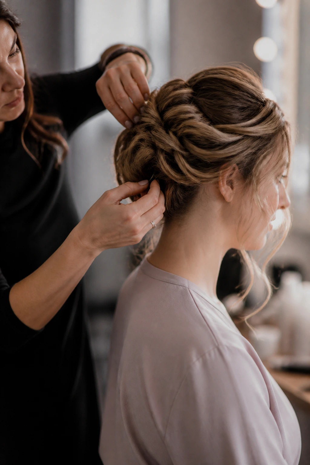 Mid-shot of a real woman with an updo being prepped by a stylist in a backstage salon