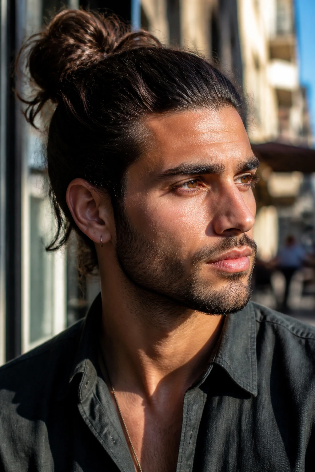 Close-up portrait of a man with a bun in a sunlit cafe