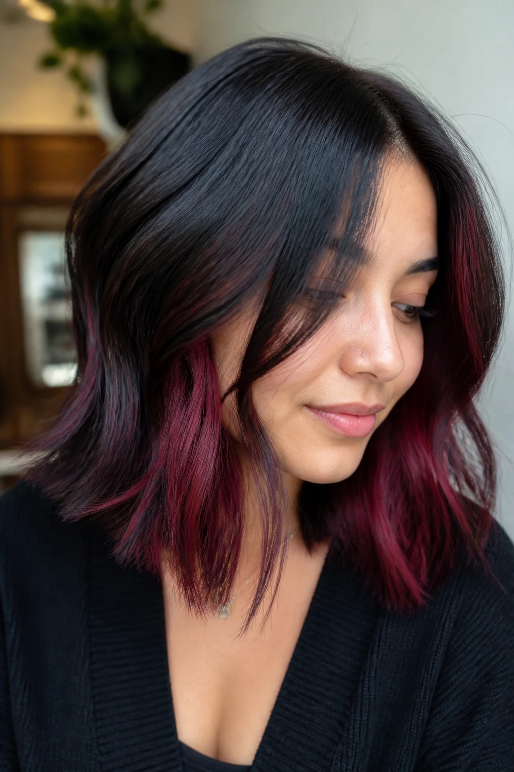 Close-up of a real woman with shoulder-length hair showing burgundy peekaboo panels beneath a dark top layer
