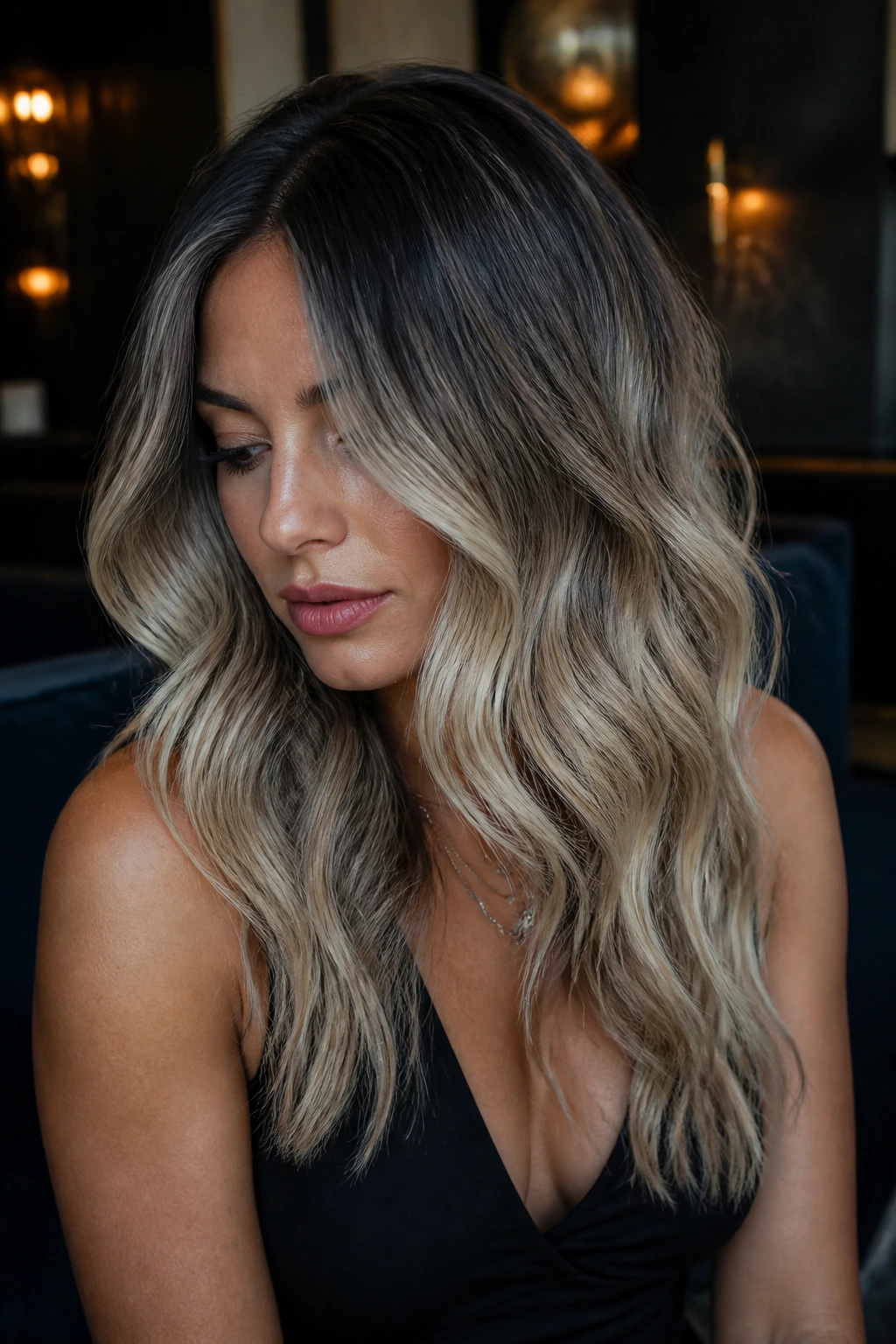 Portrait of a real woman with charcoal blonde melt showing charcoal roots fading into smoky blonde