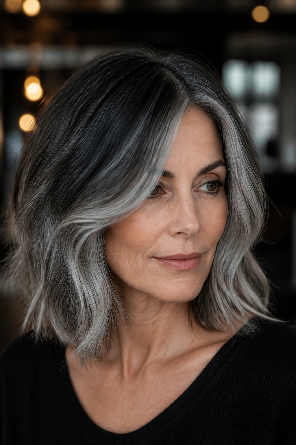Close-up of a real woman with charcoal-root melt on shoulder-length hair.