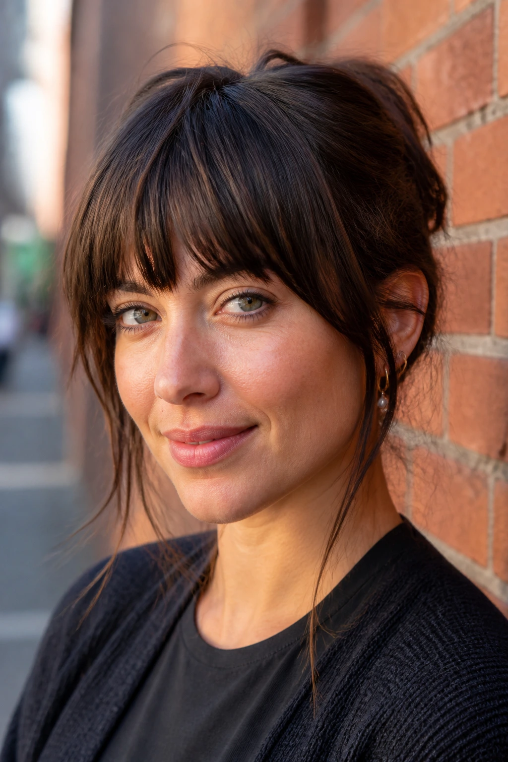 Close-up of a real woman with choppy thick bangs by a brick wall
