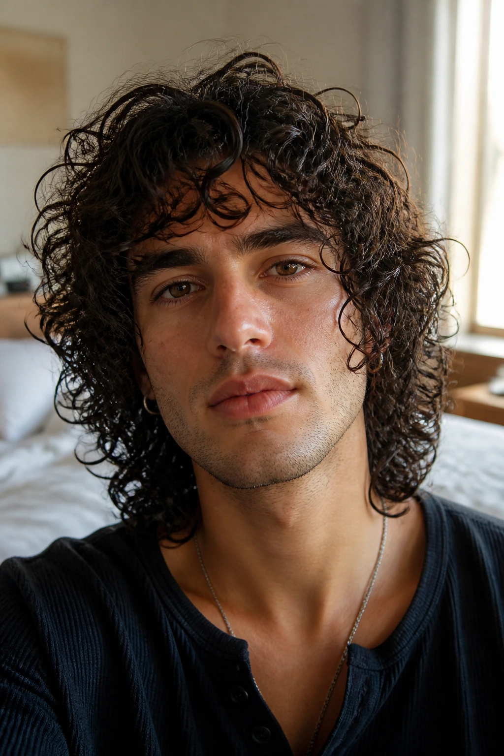 Close-up portrait of a real man with curly mop hairstyle in a softly lit bedroom.