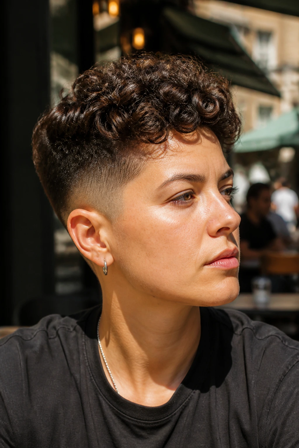 Close-up portrait of a real person with a curly top fade in a sunlit street cafe