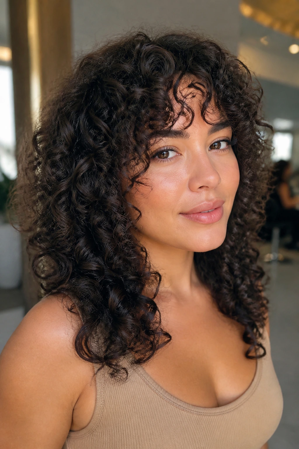 Close-up portrait of a real woman with Deva Cut face-framing bangs in a sunlit salon