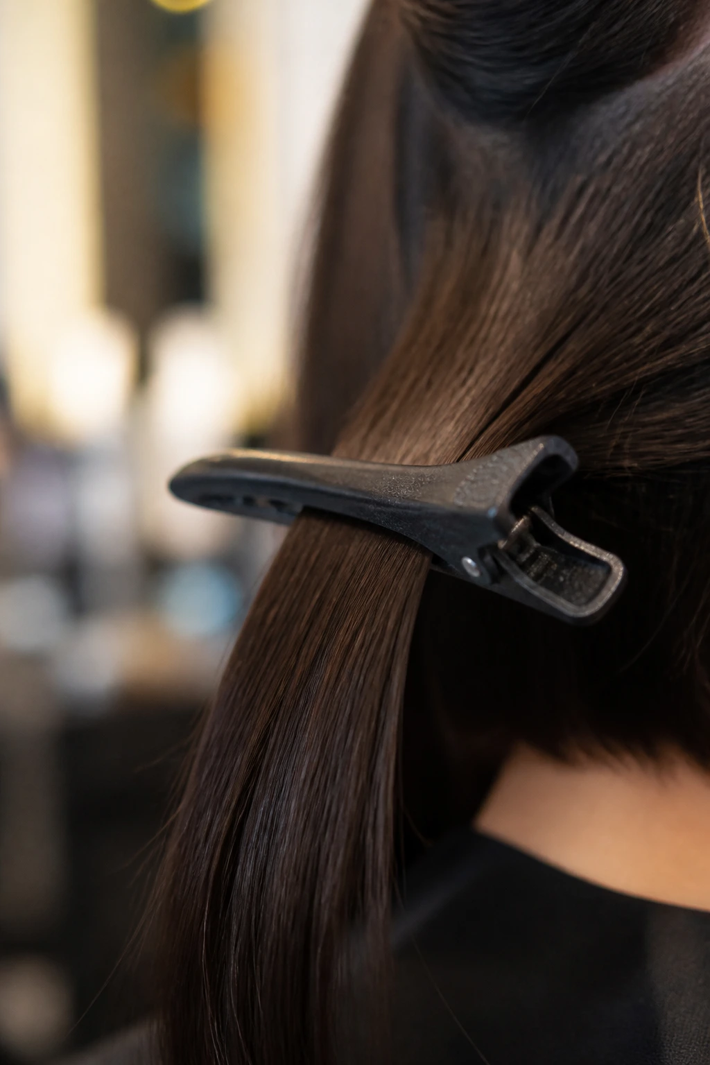Macro close-up of a duckbill clip used for lob styling in a salon