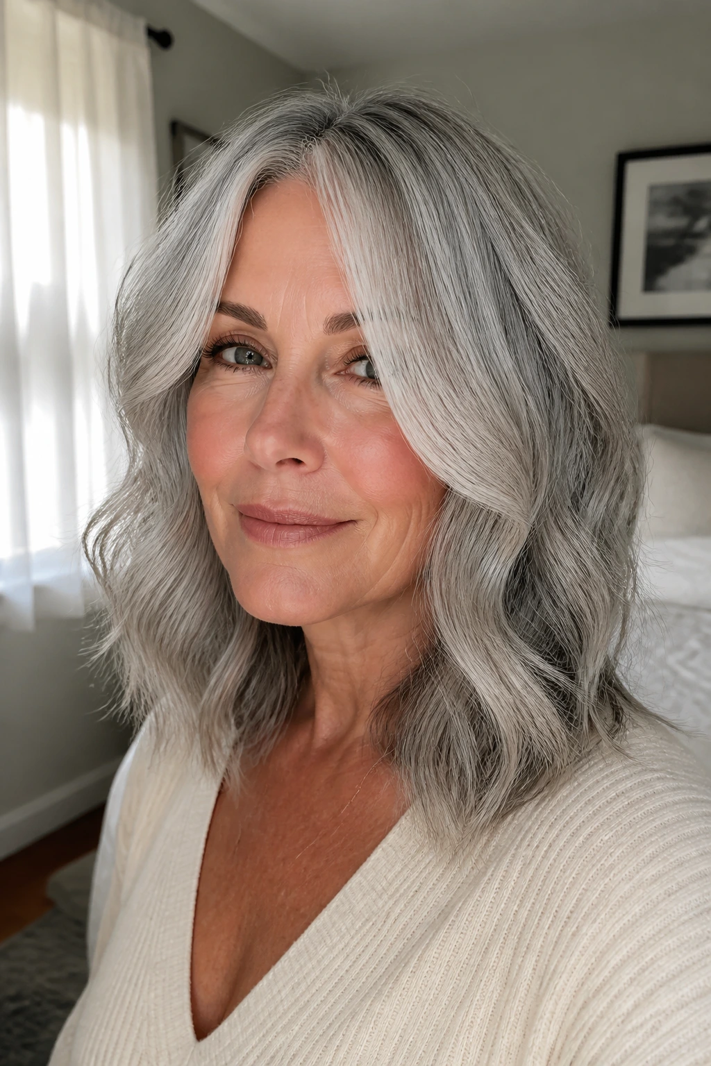 Medium close-up of a real person with face-framing layers and loose waves in gray-silver hair