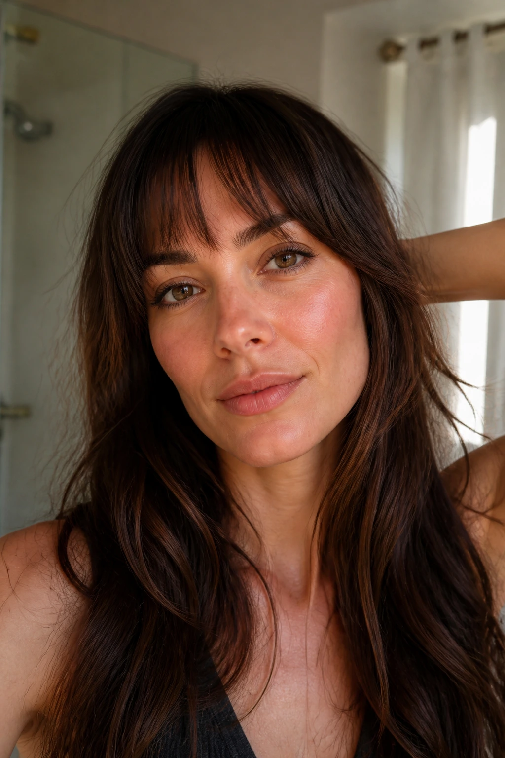 Close-up portrait of a real woman with long bangs, showing fringe maintenance in a softly lit bathroom setting