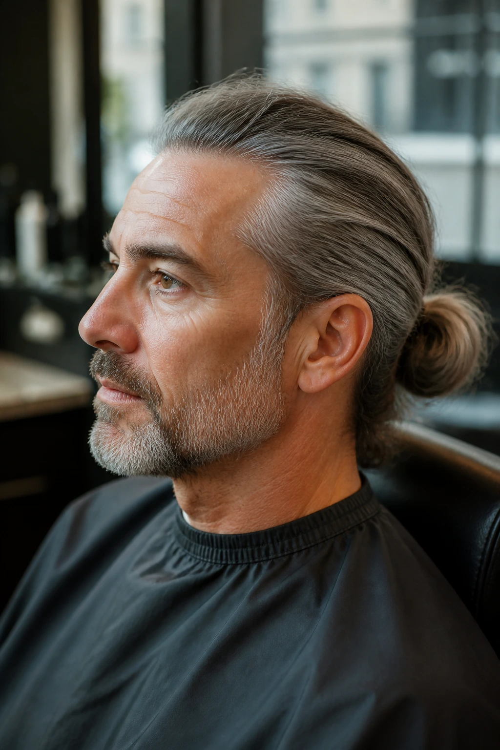Close-up of a man with a gray man bun in a salon chair