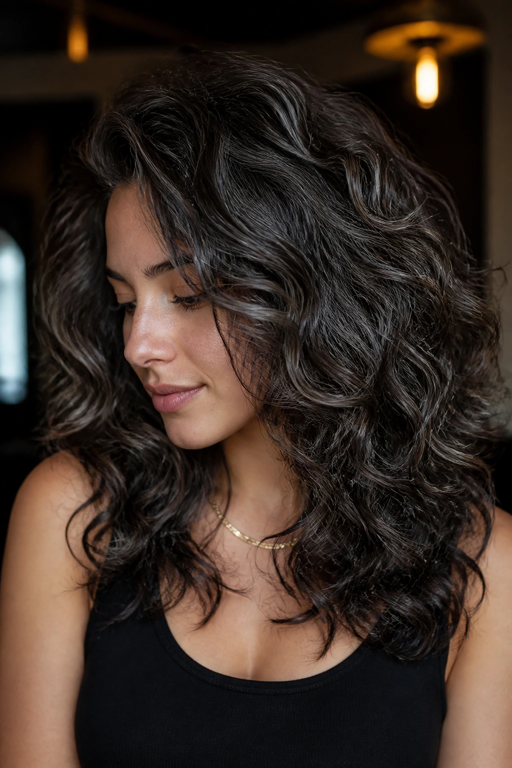 Dark brunette curls with gunmetal veil balayage for a moody look.