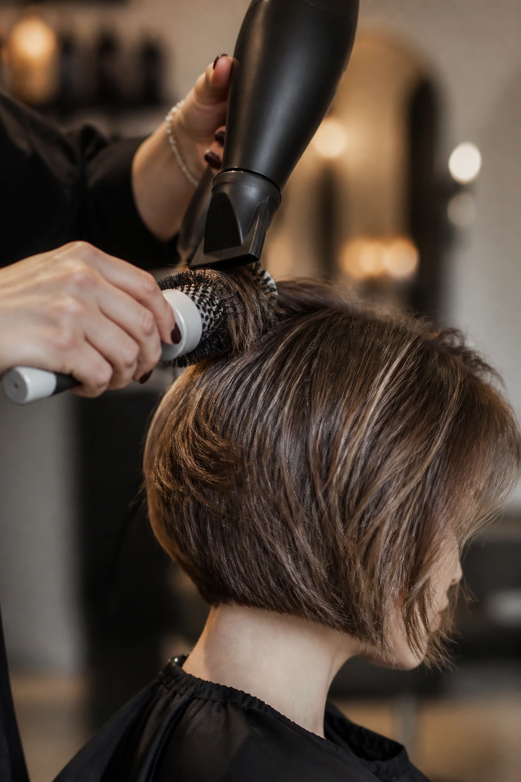 Close-up of a stylist using a blow dryer and round brush on thick hair in a salon.