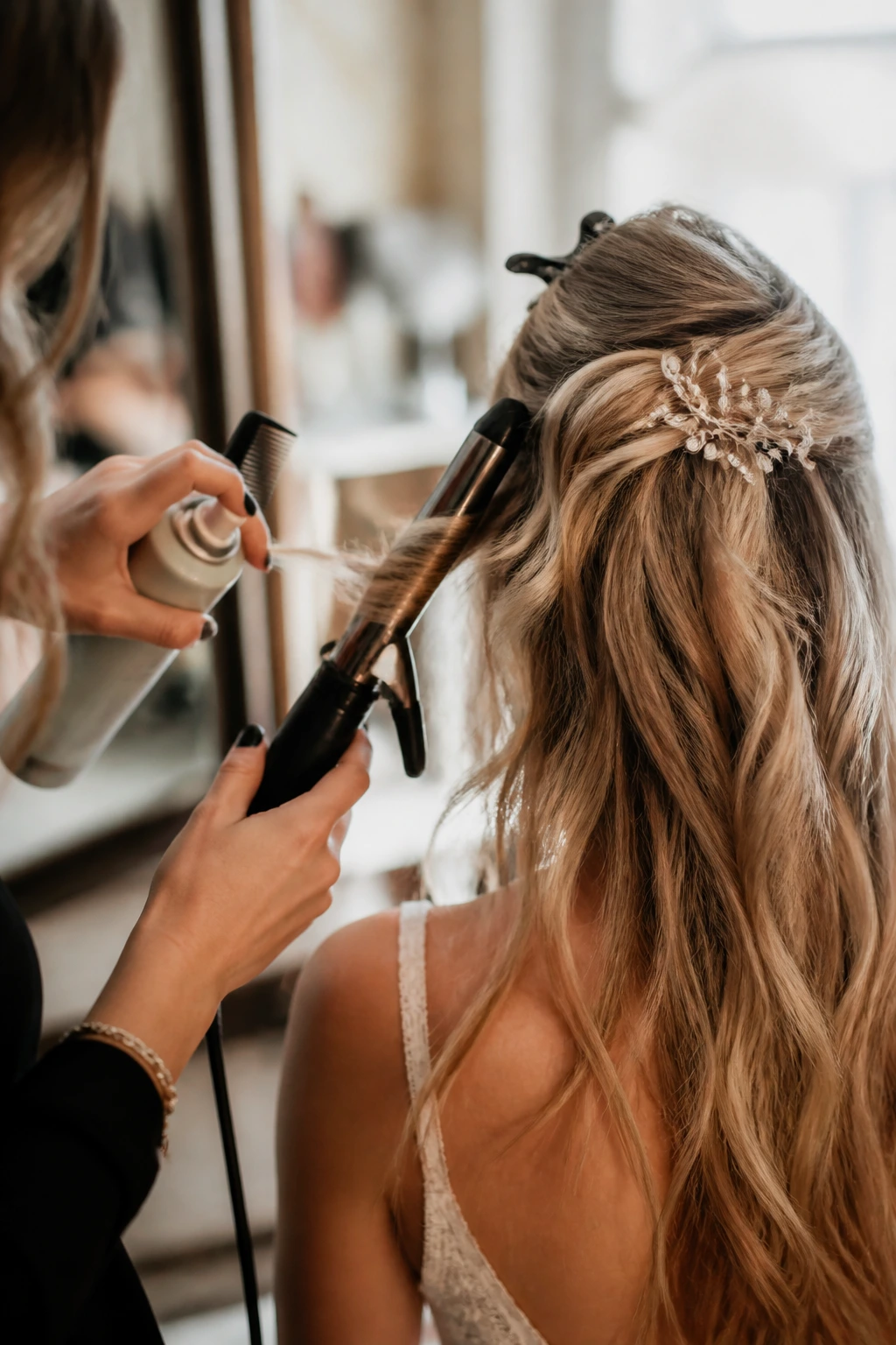Hands styling hair with curling wand on a bride.