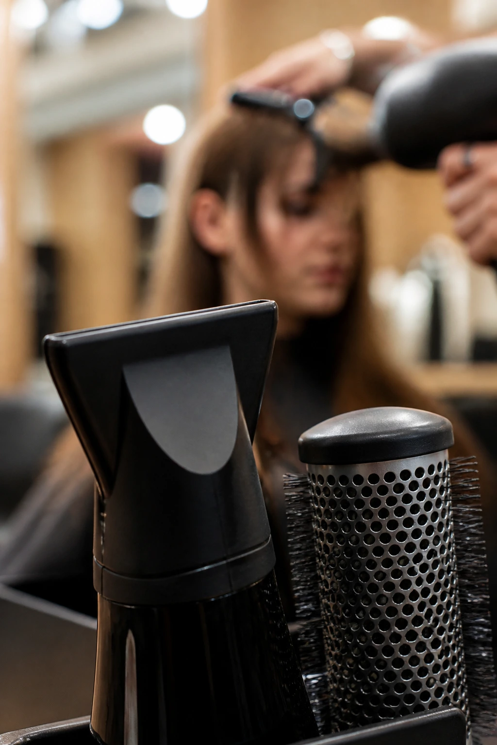 Close-up of hair styling tools with a blurred stylist in a salon