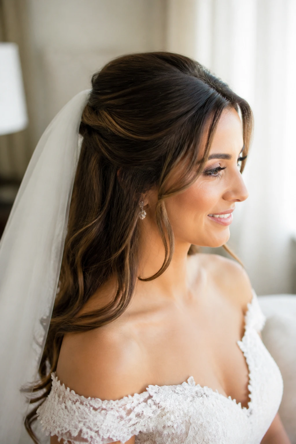 Close-up portrait of a bride with half-up bridal hair, veil at the crown, and off-shoulder neckline.