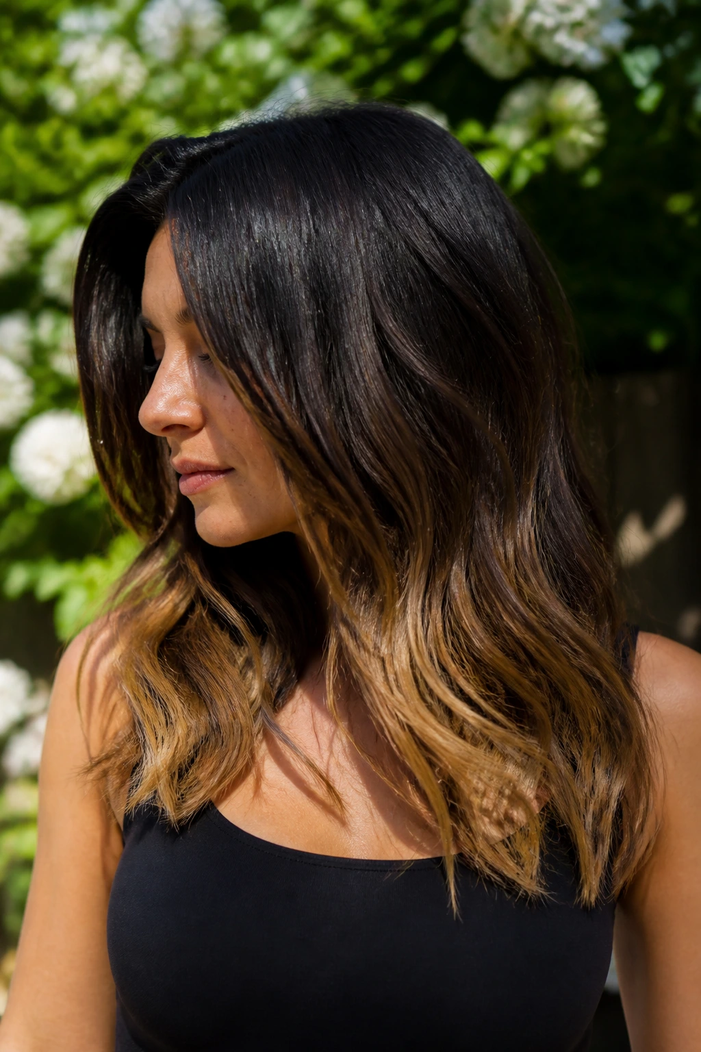 Close-up of a real woman with dark hair and honey-dipped ends catching sunlight.