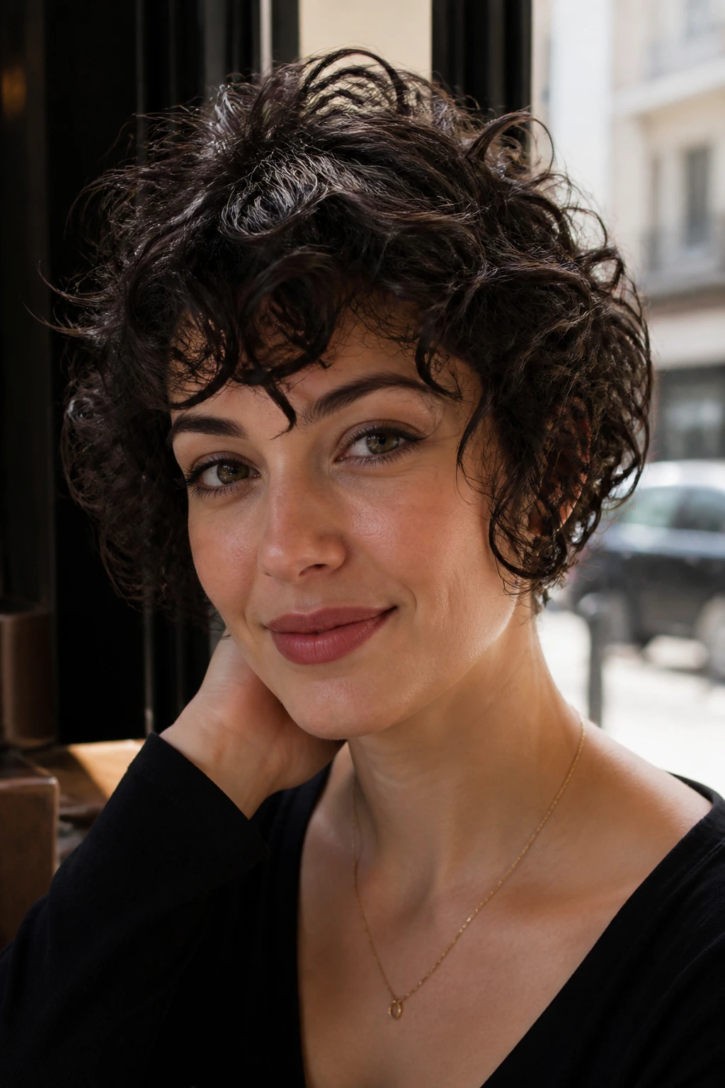 Close-up of a real woman with jaw-length curly pixie by cafe window.