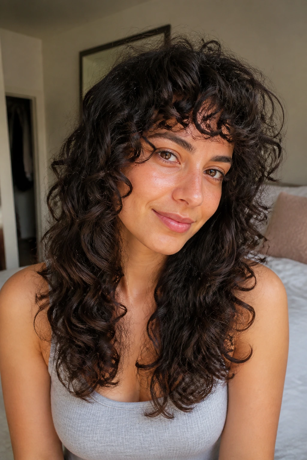 Real person with long curly hair featuring layered ends that flip, in warm bedroom light