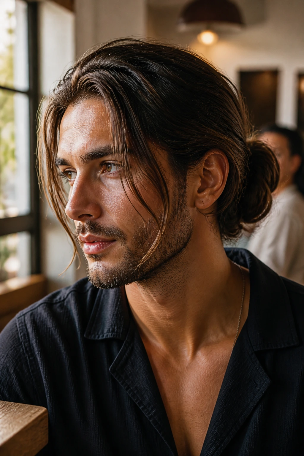 Close-up of a man with a low bun and face-framing pieces in warm cafe light