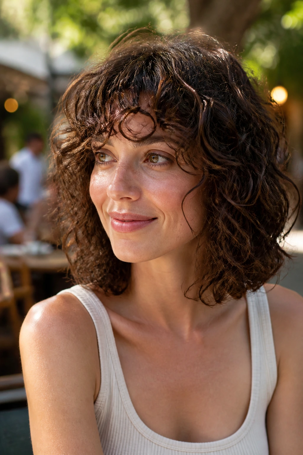 Portrait of a real person with an airy micro-layer bob and light, buoyant curls in a sunlit courtyard.