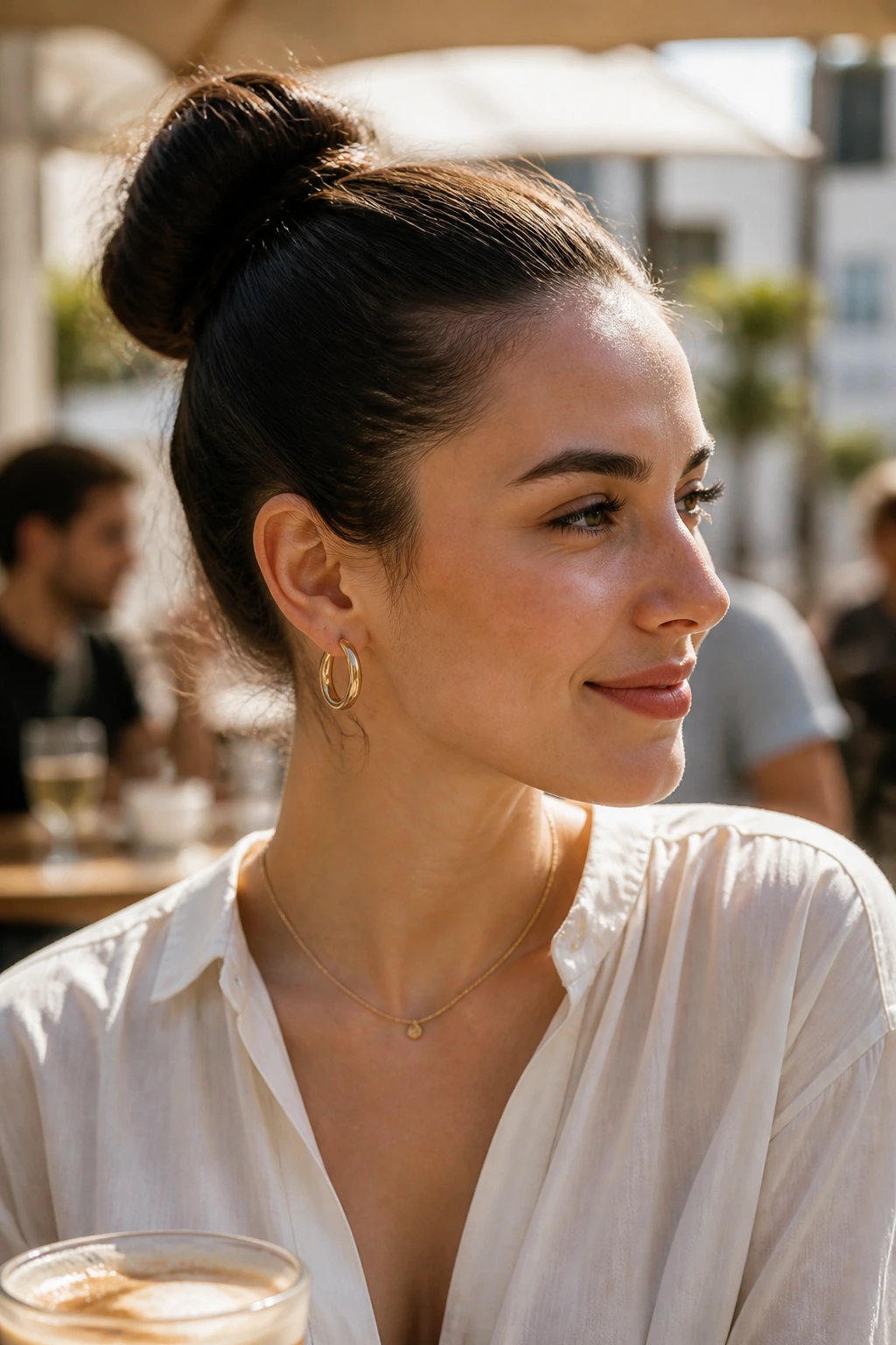 Portrait of a woman with a neat bun outdoors in a sunlit cafe.