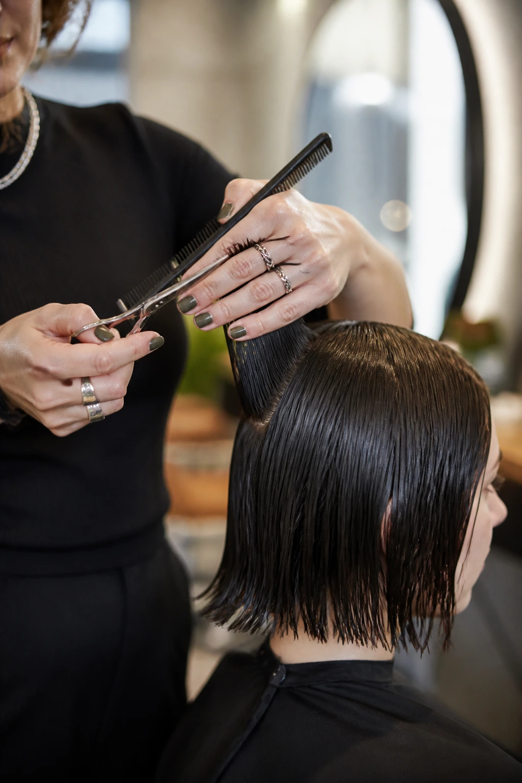 Hairstylist hands using scissors and comb on damp hair on a real client in a salon