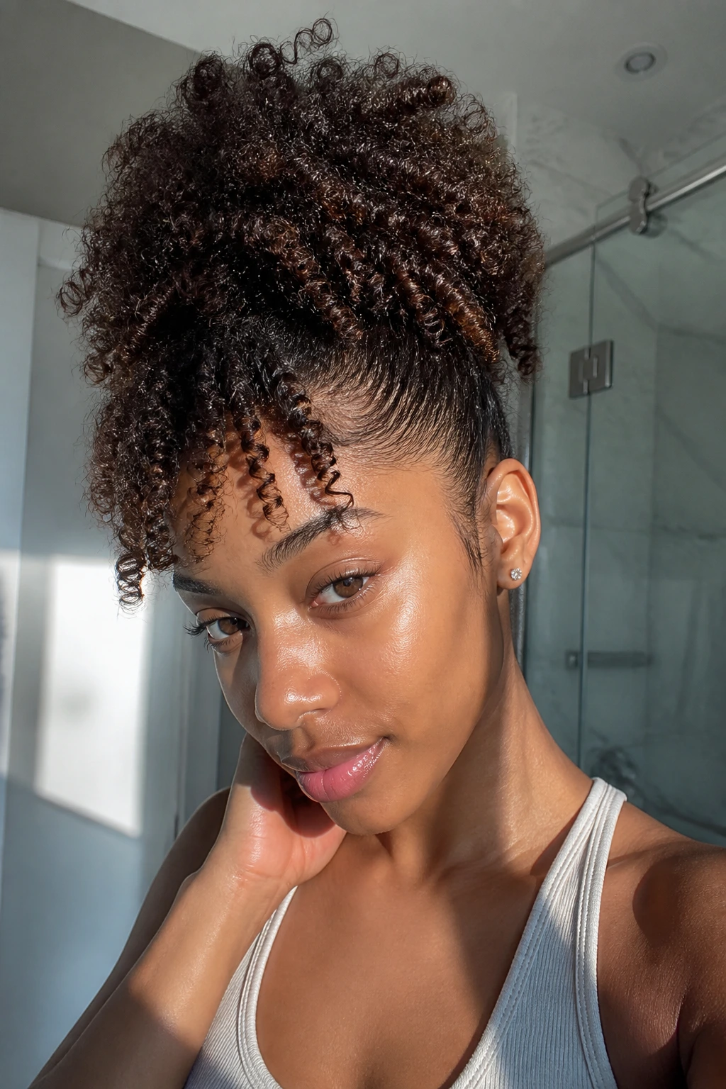 Close-up of a real woman with a high pineapple puff and forward curls in warm bathroom light