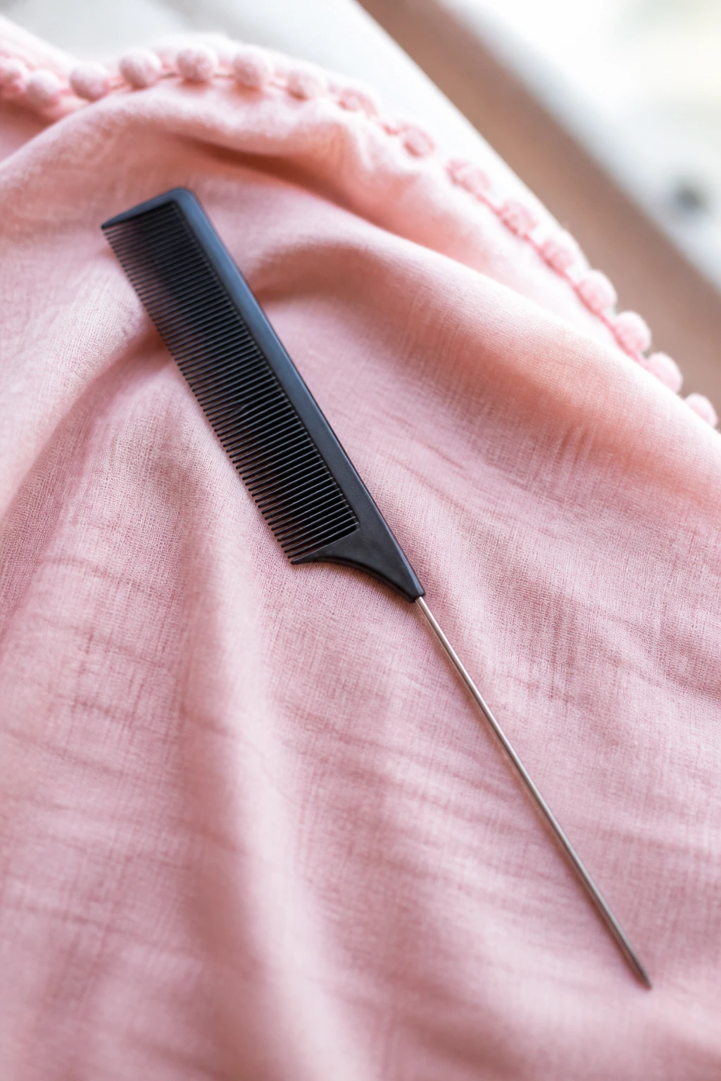 Close-up of a rat-tail comb on pastel fabric