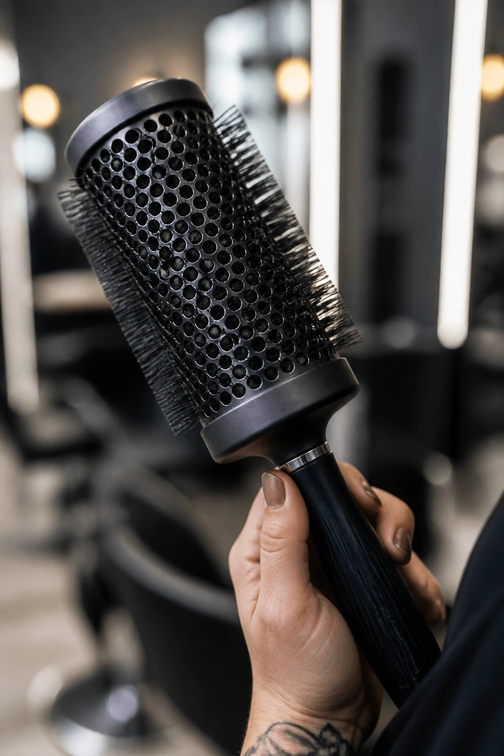Close-up of a round brush in a stylist's hand in a salon.
