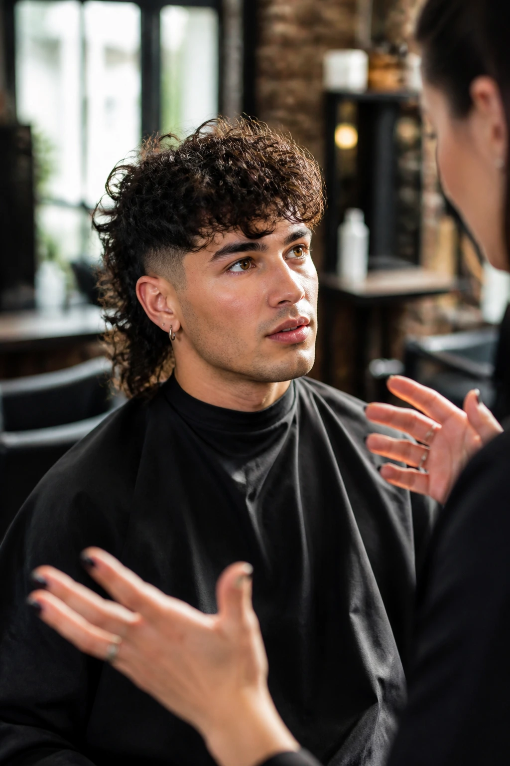 Close-up portrait of a person with curly hair in a salon chair discussing haircut details with a stylist.
