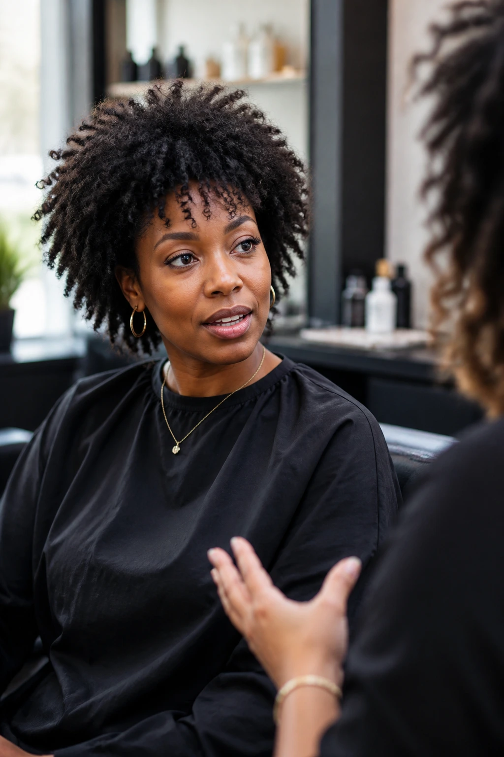 Portrait of a client in a salon chair discussing haircut details with a stylist.