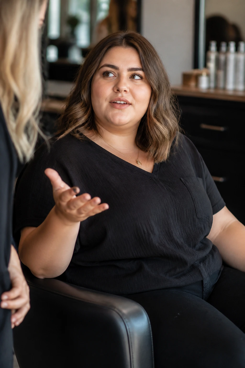 Woman in a salon chair discussing hairstyle options with a stylist