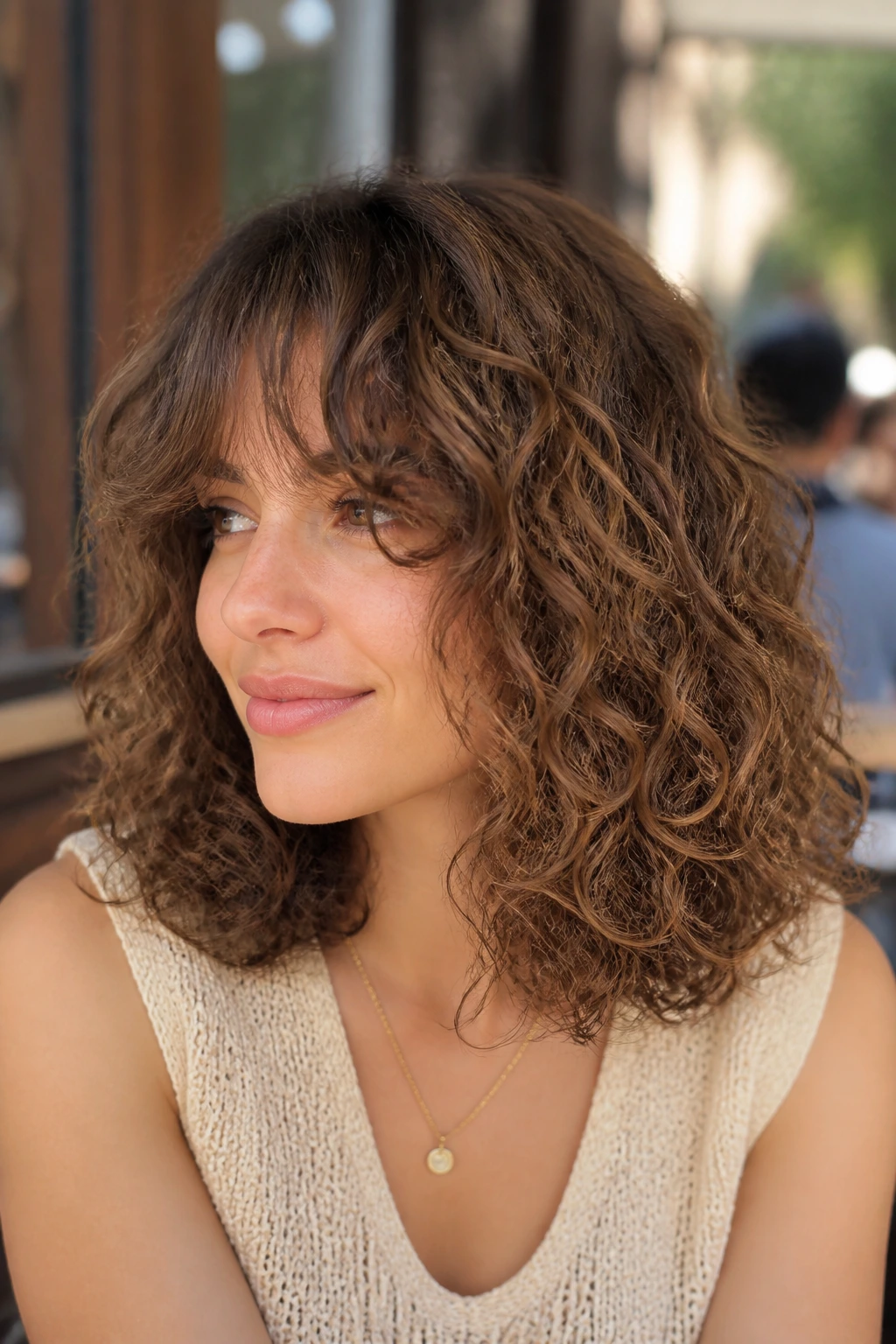 Portrait of a woman with shoulder-skimming curls and a long fringe in sunny outdoor cafe