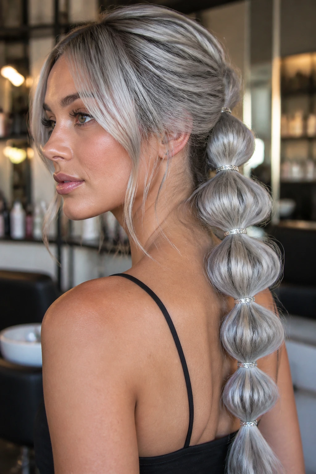 Real person with long silver-gray bubble braids in a warm-lit salon