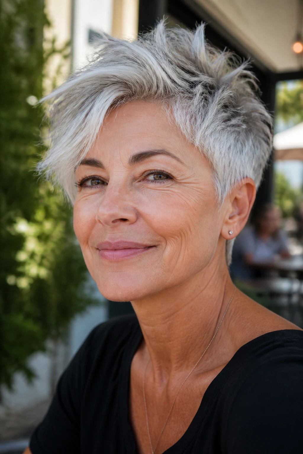 Close-up portrait of a person with a tousled silver pixie and longer top in sunlight.