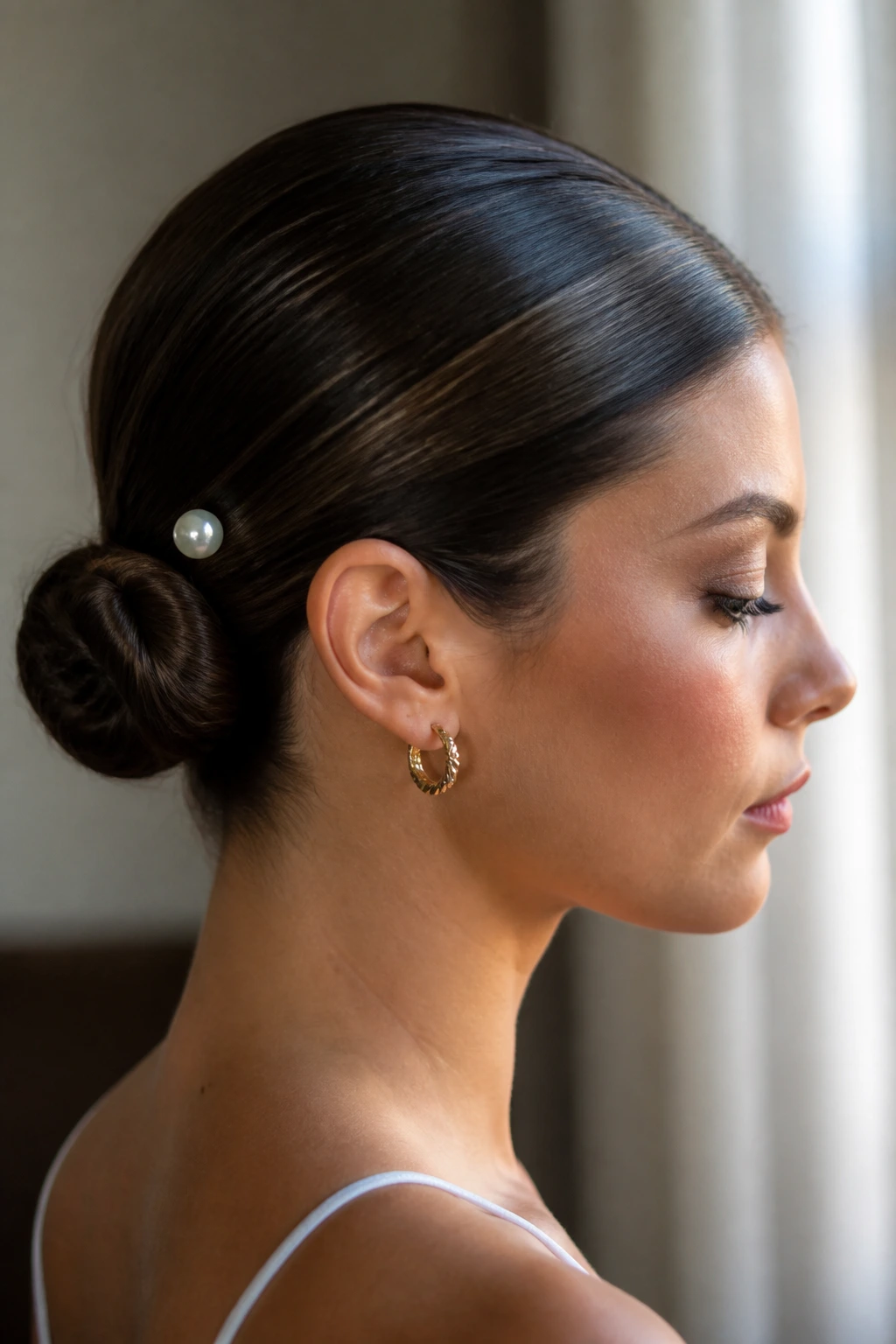 Close-up of a woman with a slicked-back bun and pearl pin hairstyle.