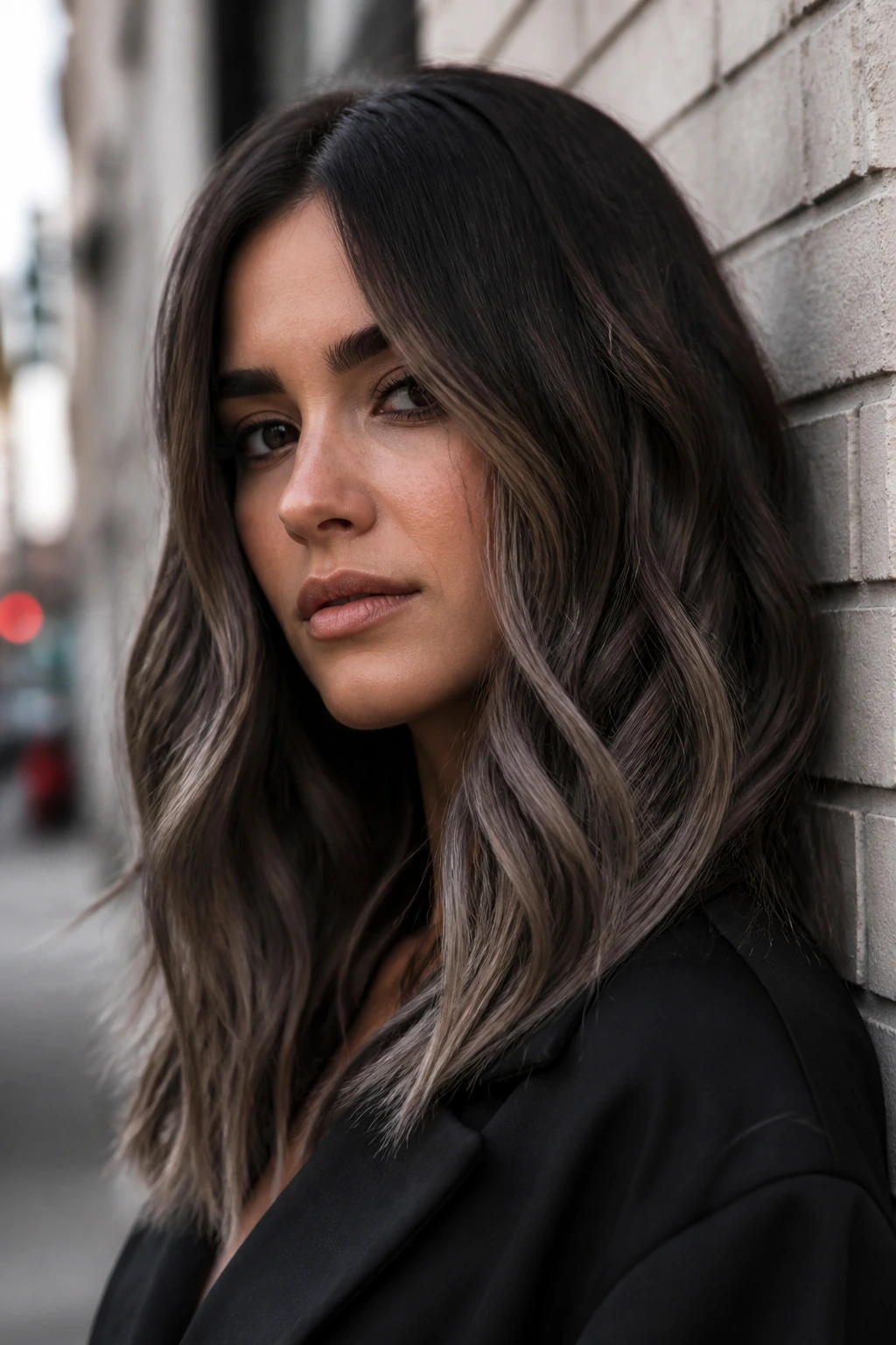 Portrait of a person with smoky brunette ombré hair against a neutral brick wall