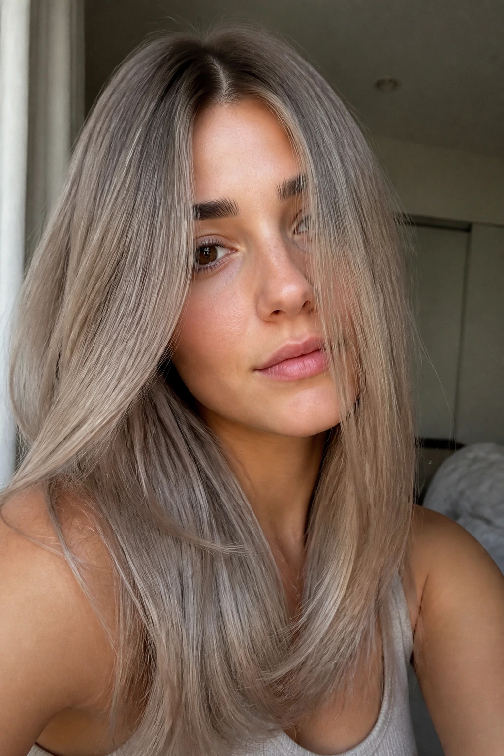 Close-up of real woman with soft mushroom blonde on straight hair in window light