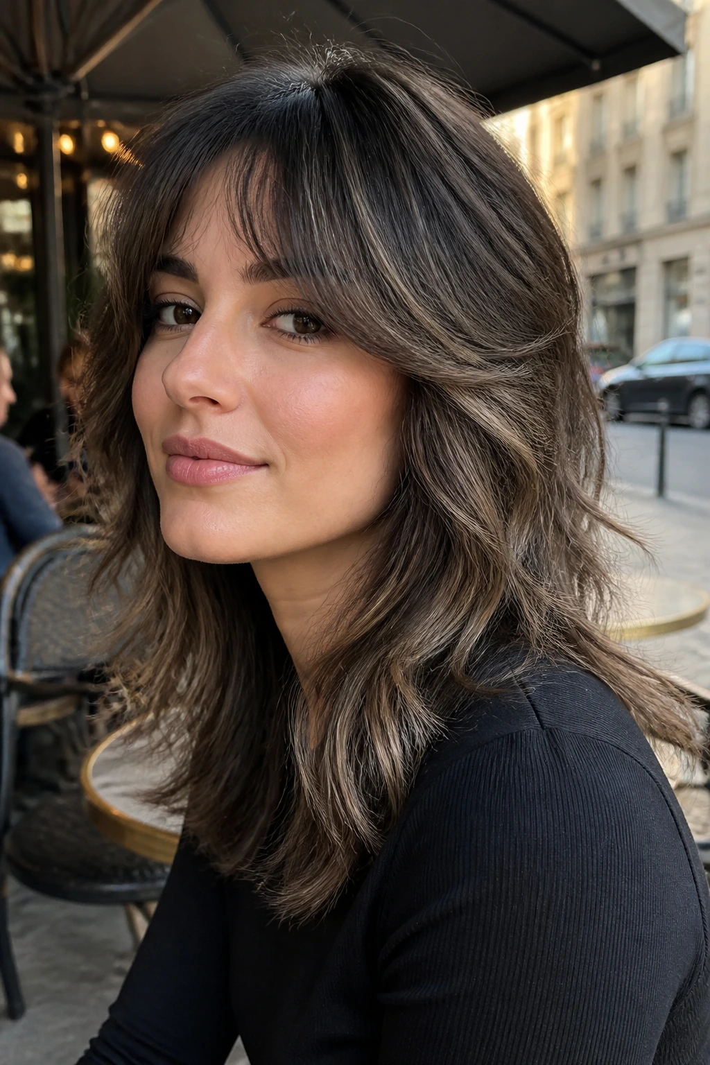 Close-up of a real woman with a soft wolf cut and ash brunette balayage in daylight.