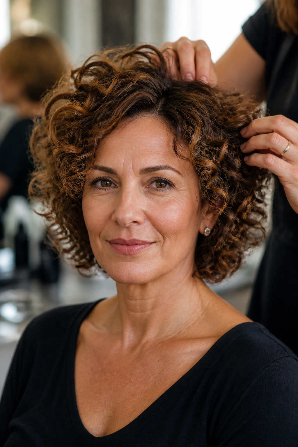 Portrait of a real woman in a salon discussing her short curly cut with a stylist nearby.
