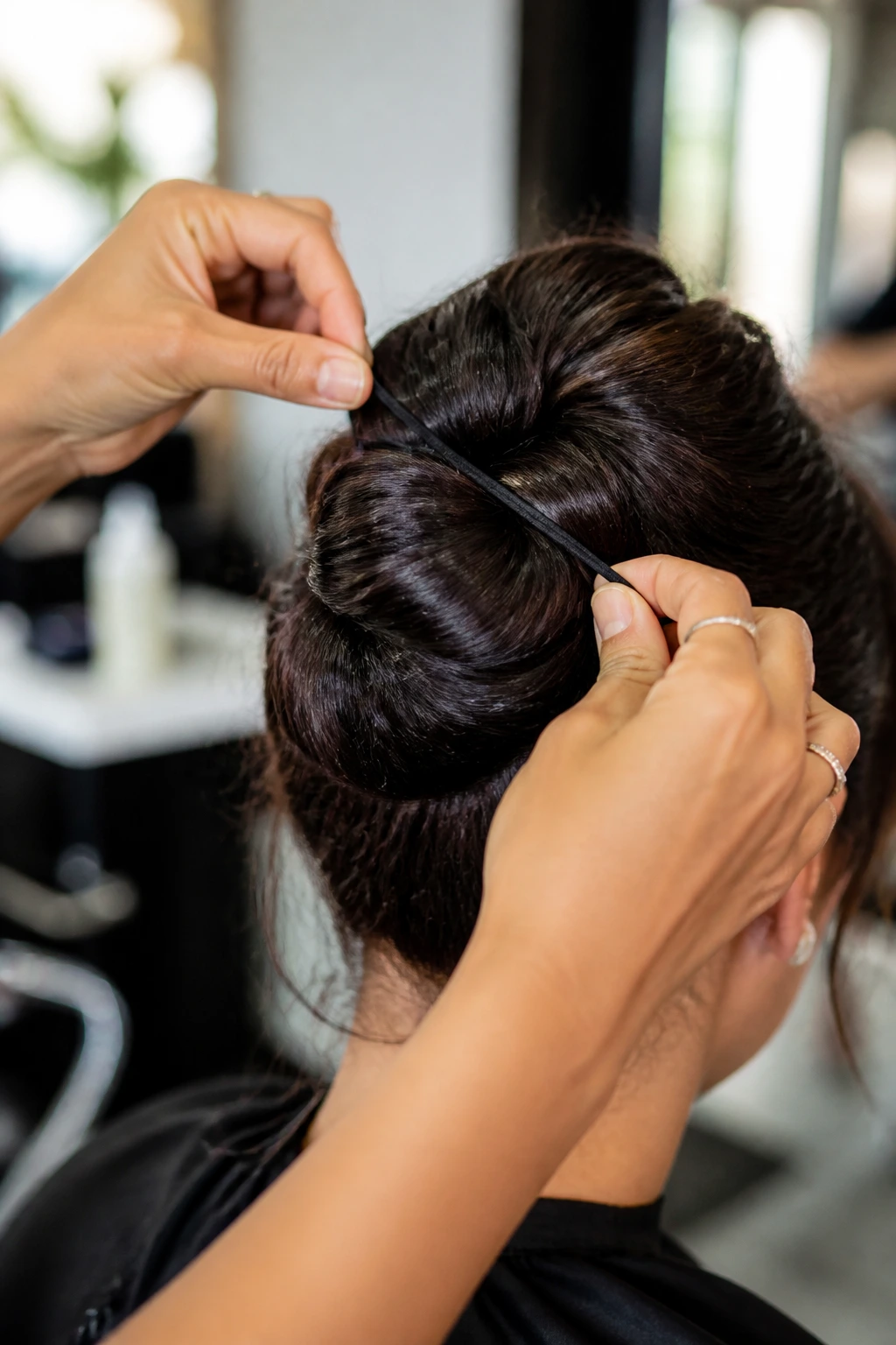 Close-up of hands fastening a coated elastic around thick hair to secure a bun in a salon setting