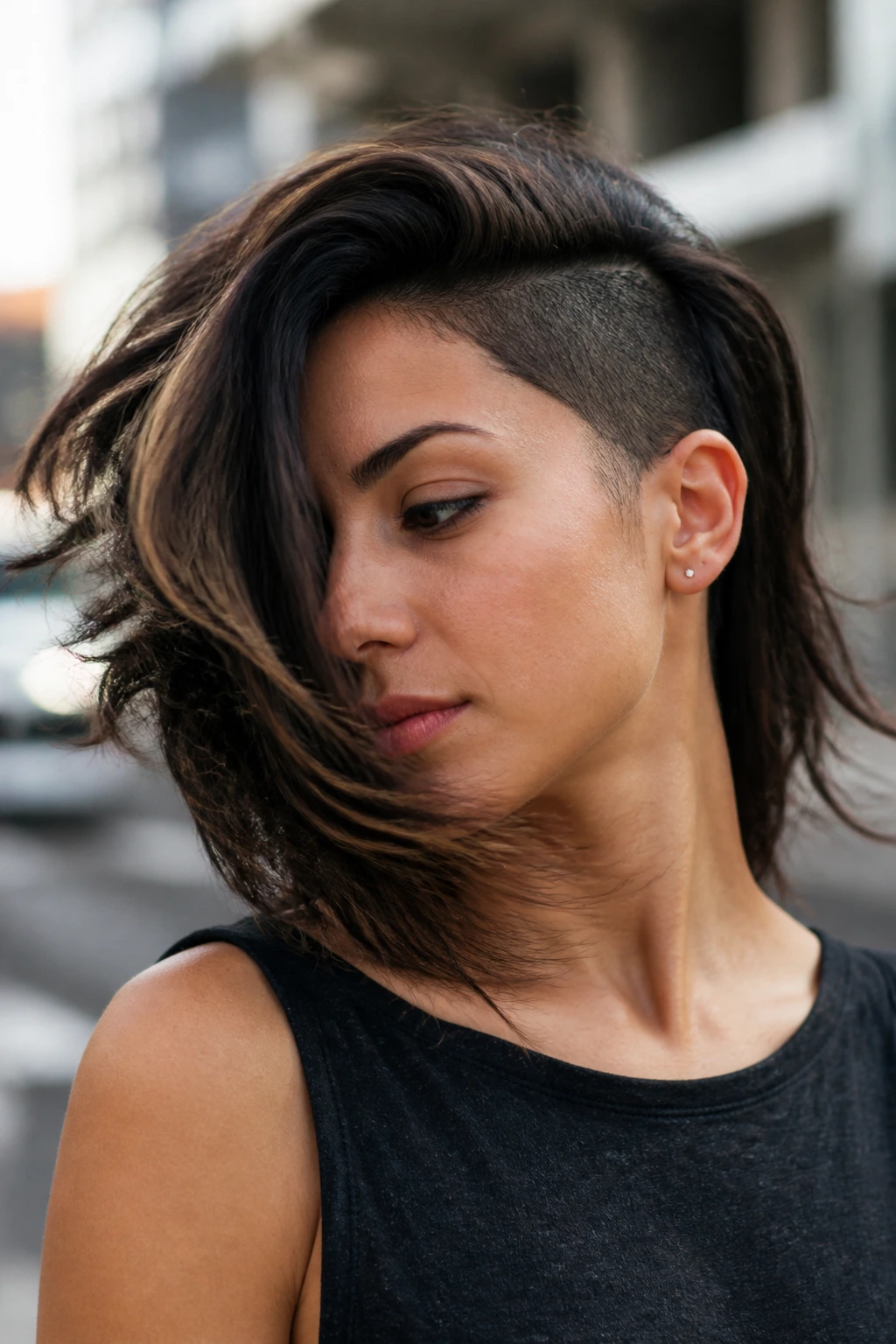 Portrait of a person with medium-length hair and an undercut, hair captured in motion against a blurred city backdrop